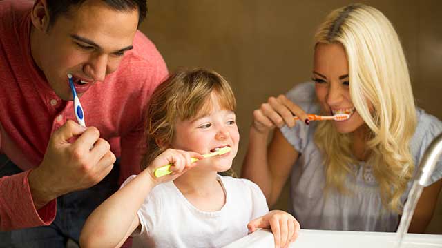 Small girl brushing teeth with her mother and father